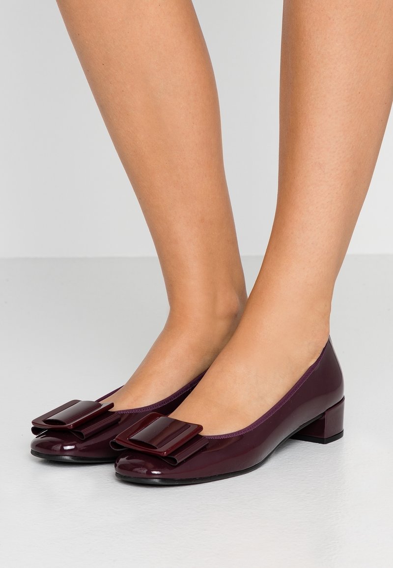 Bordové lakované baleríny se čtvercovým mašlí. Hladký špičatý tvar a malý blokový podpatek. Hladký vzhled s lesklým povrchem.