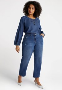 Camisa de denim con cuello redondo y detalles de botones, combinada con jeans azules de cintura alta que tienen un corte relajado y acentos desgastados.