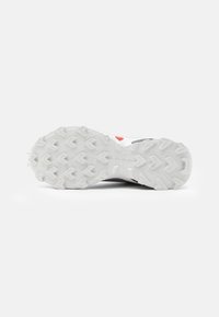Chaussure de course pour homme avec une semelle extérieure en caoutchouc blanc texturé, dotée d'un motif de semelle en forme d'hexagone et d'un dessus gris. Détail d'accent rouge présent.