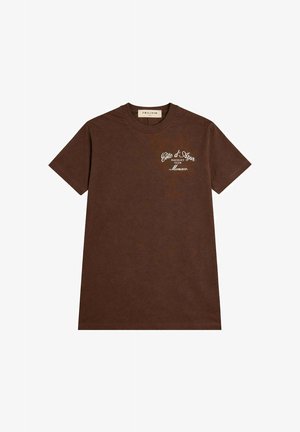 T-shirt marron à manches courtes avec col rond et inscription blanche "Côte d'Azur Racquet Club Monaco" sur la poitrine gauche.