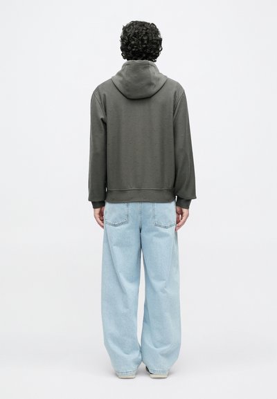 Σκούρα γκρι φούτερ με κουκούλα και υφασμάτινο σχέδιο, συνδυασμένο με ανοιχτό μπλε φαρδιά τζιν. Η εμφάνιση φαίνεται από πίσω.