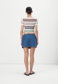 Kortermet, cropped strikket topp med flerfargede horisontale striper; kombinert med et tettsittende, denim mini-skjørt.