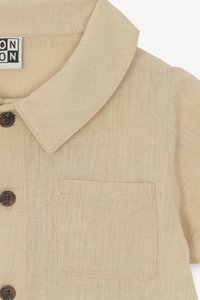 Beige linen shirt featuring a collar, front pocket, and dark brown buttons, with a textured surface for a casual look.