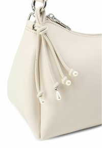 Borsa a mano in pelle beige chiaro a forma trapezoidale, con corde decorative annodate e dettagli simili a perle vicino alla cerniera.