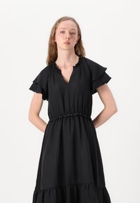 Black dress with short ruffled sleeves and a V-neckline. Features an elastic waist and a tiered, flowing skirt. Textured fabric.
