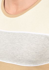 Lys beige T-shirt med rund halsudskæring; har et panel i creme og grå vandrette striber over brystet. Blød bomuldsstruktur.