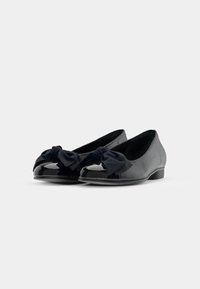 Ballerines noires avec un dessus en tissu lisse et des embouts en cuir verni brillant. Un grand nœud en tissu orne l'avant de chaque chaussure. Talon bas.