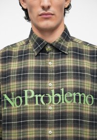 Zelená a čierna kockovaná košela s golierom na gombíky, na prednej strane s textom "No Problemo" v zelenej farbe a bielymi gombíkmi.