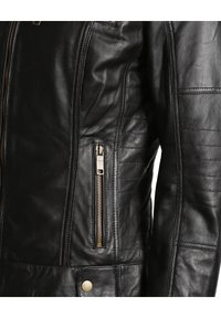 Černá kožená bunda s zipovou kapsou, prošívanou strukturou a zlatými kovovými doplňky. Hladký povrch s přiléhavým střihem.