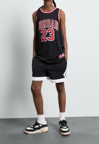 Svart mesh baskettröja med röda detaljer, med "JORDAN" och "23" på framsidan. Kombinerad med svarta shorts och svarta sneakers.