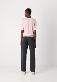 Light pink short-sleeve top with a round neckline and back seam detail, paired with loose-fitting dark grey jeans and light-colored shoes.