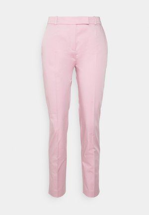 Pantalon rose clair sur mesure avec passants de ceinture, pli devant et coupe slim sur fond blanc uni.