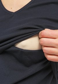 Námořnická bavlněná blůza částečně vytažená a odhalující béžovou vnitřní vrstvu. Tkanina vypadá měkká s hladkým povrchem. Viditelný detail výstřihu do V.