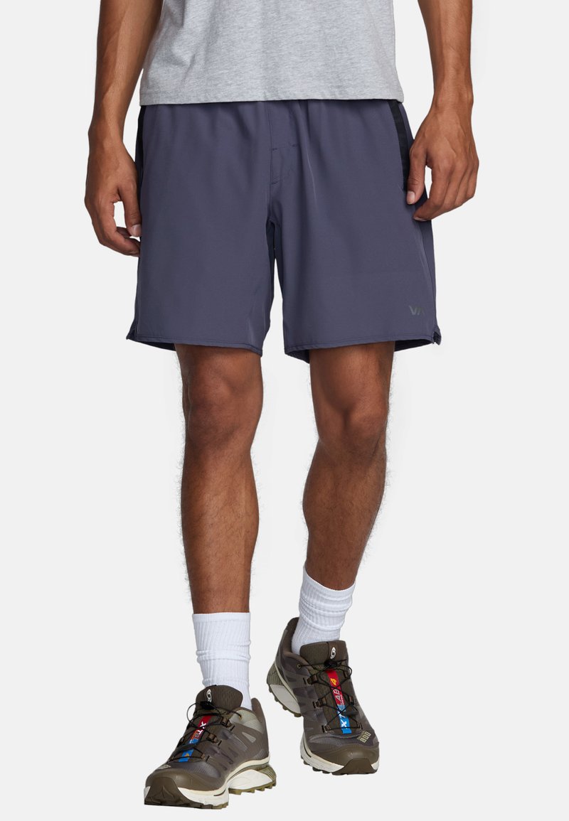 Shorts de sport bleu marine en tissu lisse, avec une taille élastique et des poches latérales, portés avec des chaussures de sport grises et des chaussettes blanches.