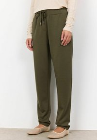 Olive green, relaxed-fit jogger pants with a drawstring waist, smooth fabric, and side pockets, paired with beige slip-on shoes.