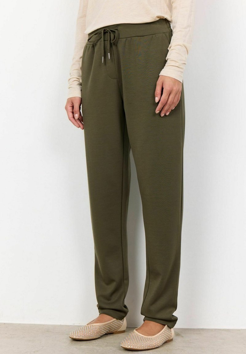 Olive green, relaxed-fit jogger pants with a drawstring waist, smooth fabric, and side pockets, paired with beige slip-on shoes.
