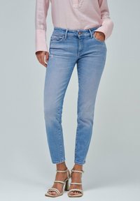 Jeans ajustados de color azul claro con cintura media, presillas para cinturón y bolsillos frontales, con un ligero desgaste en el muslo.