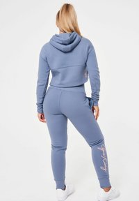 Ljusblå kort hoodie och matchande joggers i mjukt tyg. Har logotyp på joggersbenet och ribbade muddarna. Vita sneakers fulländar looken.