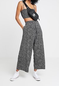 Svartvitt prickigt crop top parat med höga vida byxor. Modellen bär vita högskurna sneakers och en svart axelväska.