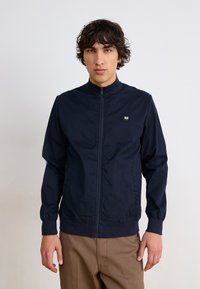 Marineblå zip-up jakke med høy krage, elastiske mansjetter og hem, med en liten logo på venstre bryst. Glatt, lett materiale.