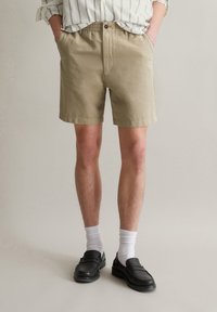 Beige cotton shorts with an elastic waistband, two side pockets, and a straight cut. Worn with black loafers and white socks.