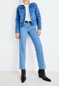 Džínová bunda s límcem z umělé ovčí vlny, modré přiléhavé džíny a černé kotníkové boty. Obsahuje knoflíky, přední kapsy a rovný střih.