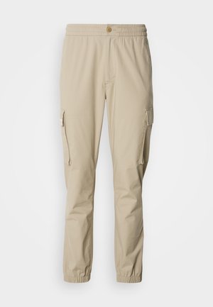 Beige cargo bukser med elastisk talje, knaplukning, sidelommer og elastiske manchetter ved anklerne, lavet af letvægtsstof.