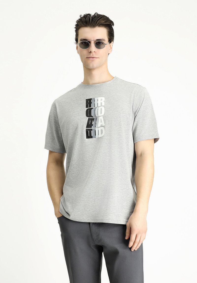 Camiseta de manga corta gris con texto gráfico vertical en negro, gris y blanco. Tejido de algodón suave, corte relajado y cuello redondo.
