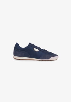 Navy blue low-top sneaker with mesh and suede upper, white textured toe cap, white midsole, brown tread sole, and side metal brand label.