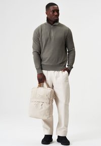 Grauer gestrickter Pullover mit einem Viertel-Reißverschluss, kombiniert mit cremfarbigen weiten Hosen und einem weichen beigefarbenen Rucksack mit verstellbaren Trägern und zwei Knöpfen.