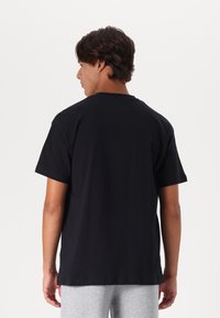 Zwarte katoenen t-shirt met een ronde hals en korte mouwen, zichtbare stiksels en een relaxte pasvorm, gedragen met grijze broek.