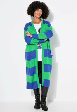 Green and blue striped long cardigan with ribbed texture, open front, and two front pockets, paired with black leggings and embellished boots.