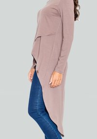 Haut taupe long et asymétrique avec des manches longues, en tissu doux et au design superposé, associé à un jean skinny bleu foncé.