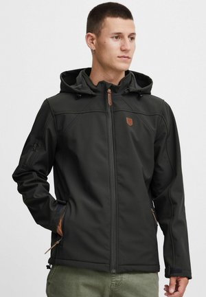 Chaqueta softshell de color verde oscuro con capucha, cierre de cremallera, dos bolsillos laterales y una tela texturizada. Presenta un parche con el logo y puños ajustables.