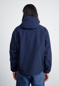 Veste imperméable bleu marine avec une capuche, des poignets élastiques et une coupe décontractée. Texture lisse et design minimaliste.