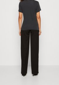 Camiseta gris de manga corta combinada con pantalones anchos negros, con una textura suave y un diseño a medida, vista desde la parte trasera.