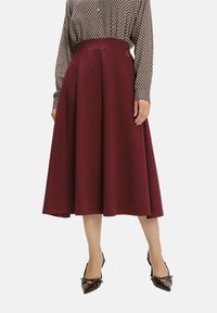 Bordeaux-farbenen Midirock mit glatter Textur, plissiertem Design und elastischem Bund. Kombiniert mit spitzen, dunkel glänzenden Lackleder-Pumps.