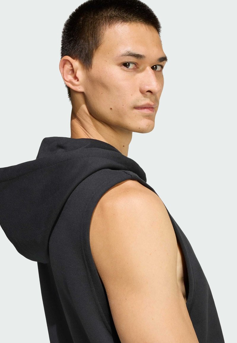 Black sleeveless hoodie with a hood, featuring a soft texture and simple design. The fabric appears lightweight, suitable for casual wear.