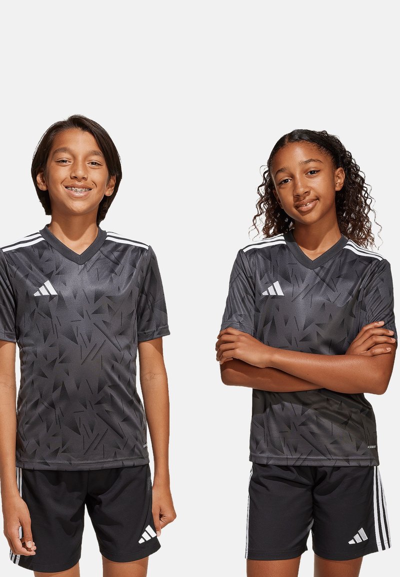 Graue Sporttrikots mit angularm Muster, schwarze Shorts und weiße Streifen auf den Schultern. Der Stoff wirkt leicht und atmungsaktiv.