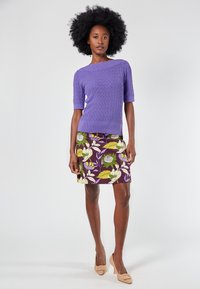 Lilac short-sleeve knit top with a textured pattern, paired with a purple floral print skirt featuring green and yellow accents. Beige heels.