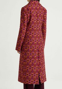 Cappotto lungo multicolore con motivo geometrico in rosa, arancione e viola, con colletto a risvolto e dettaglio con spacco laterale.