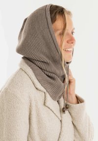 Geribbelde grijze gebreide capuchon met verstelbare trekkers en houten kralen, gedragen over een lichtbeige gestructureerde jas.