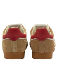 Le sneaker in suede presentano un corpo color beige con dettagli in pelle rossa sul tallone, sulla linguetta color beige e una striscia laterale bianca. La suola in gomma offre trazione.