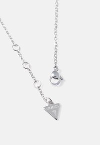 Collana in argento con anelli circolari, dotata di un ciondolo triangolare con incisione "GUESS" e chiusura a moschettone.