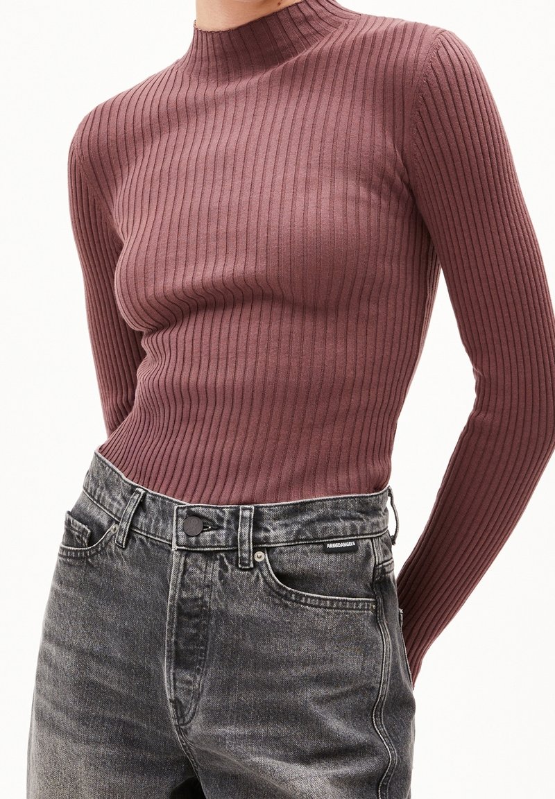 Col roulé mauve côtelé ajusté à manches longues, associé à un jean en denim noir délavé taille haute avec poches avant et fermeture à boutons.