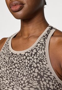 Pruunist mustriga tops, millel on ümar kaelus. Materjal on pehme, tekstuuriga ning sellel on graafiline kujundus ebaregulaarsetest kujudest tumedamates toonides.