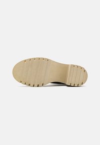 Czarna podeszwa trampka z gładkim, beżowym bieżnikiem z gumy. Posiada pionowe rowki i zaokrąglony czubek. Czysty design z minimalnym detalowaniem.