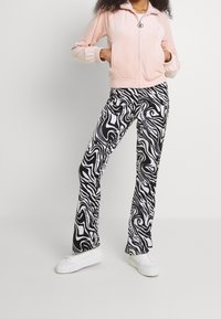 Rosa velourjacka med dragkedja och ribbade muddar, kombinerad med svartvita utsvängda byxor med virvelmönster och vita sneakers.