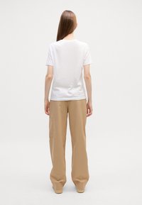 T-shirt bianco a maniche corte in tessuto di cotone, abbinato a pantaloni beige larghi con tasca laterale; entrambi hanno una vestibilità rilassata e una texture morbida.
