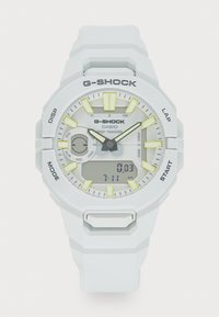 Montre G-SHOCK blanche avec un affichage numérique, des accents jaunes, un bracelet en caoutchouc texturé et un boîtier rond. Comprend des fonctions de suivi des pas.